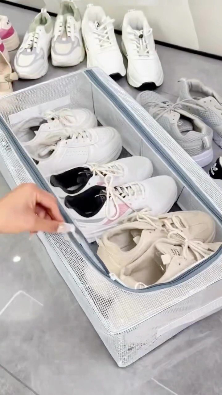 A hand zips a mesh organizer filled with white sneakers on a tiled floor.