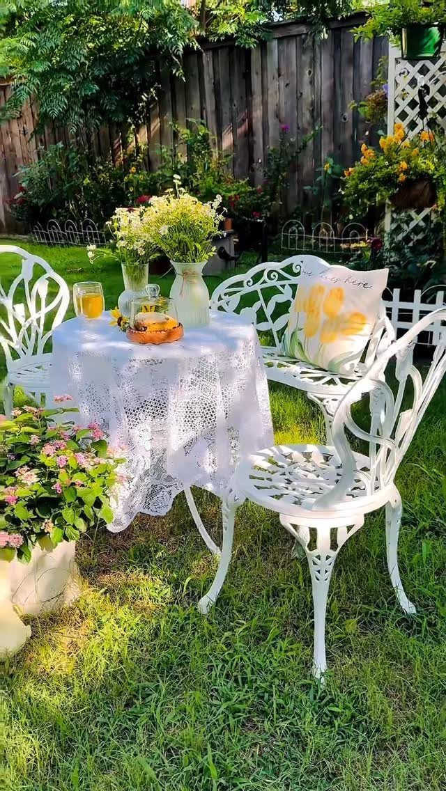 18 Small Backyard Garden Ideas for Compact Outdoor Style 7 White metal bistro set with lace tablecloth and flowers on a green lawn.