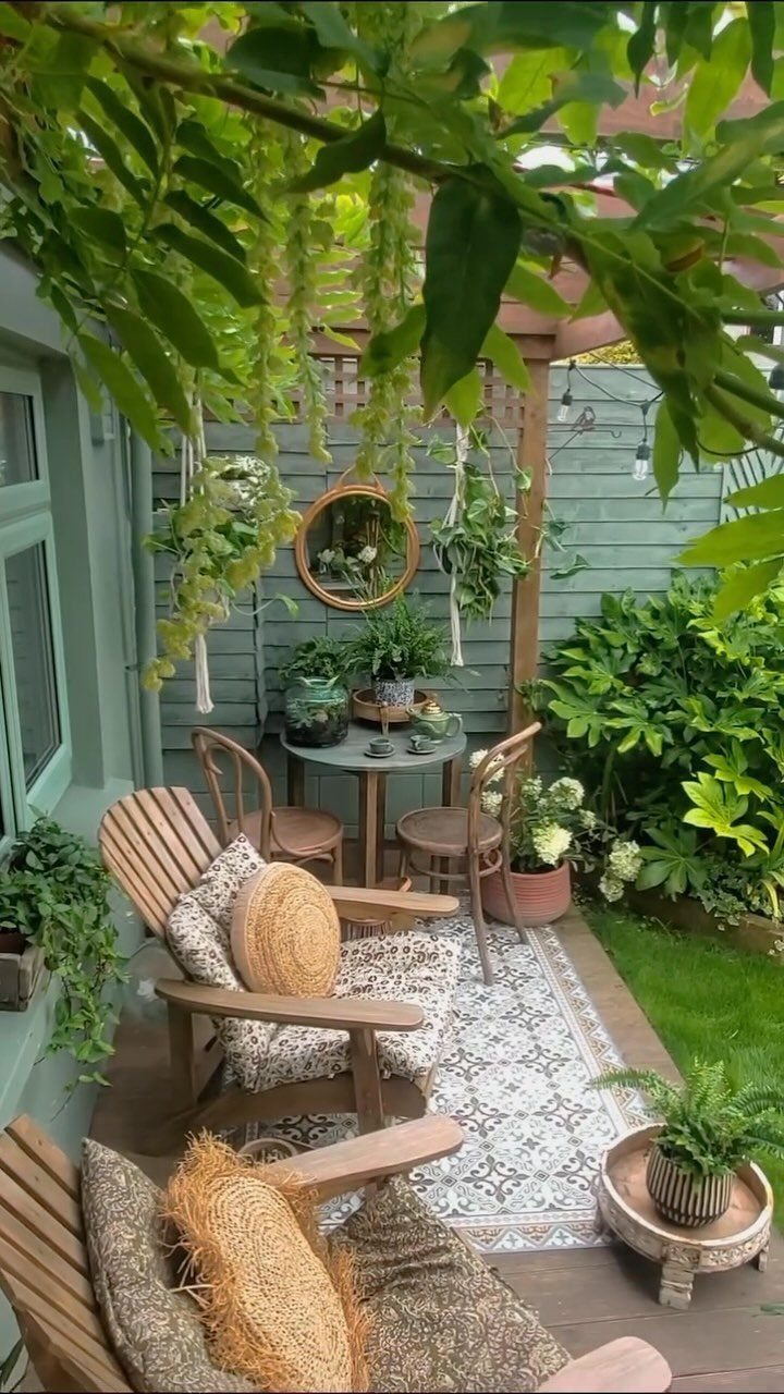 Wooden patio chairs with patterned cushions and a small table set on a patterned rug surrounded by greenery.