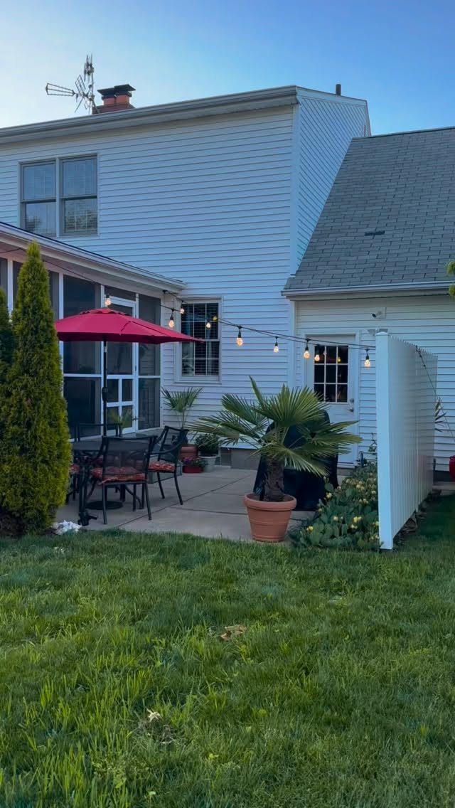 String lights hanging across a backyard patio with a red umbrella and outdoor furniture.