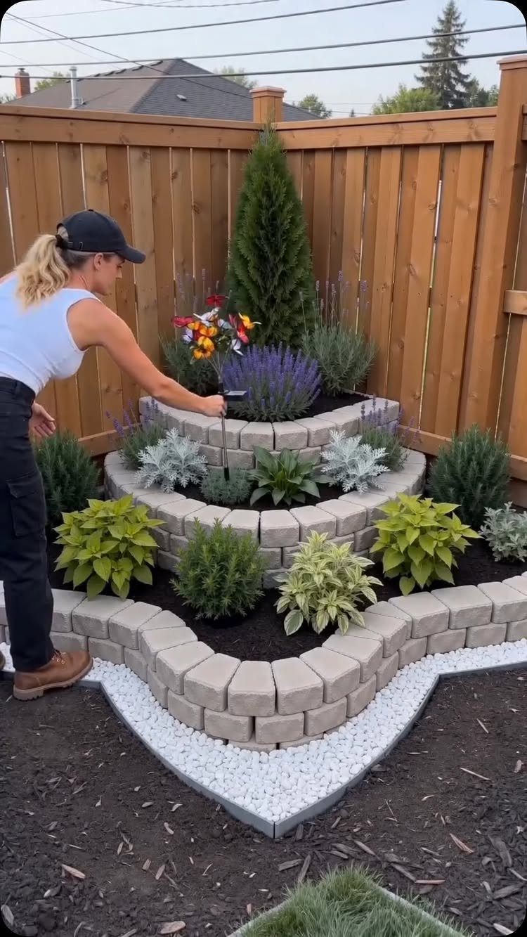 A woman gardening in a tiered stone planter filled with colorful flowers and green shrubs.