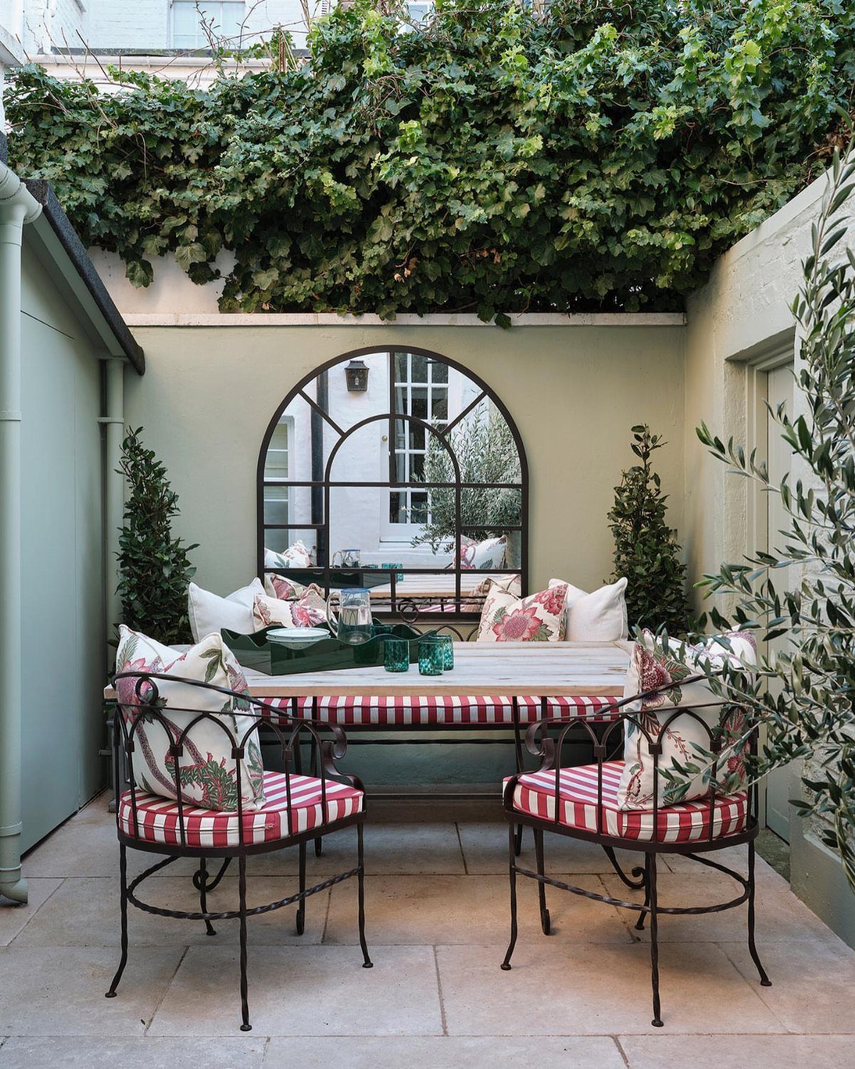 Arched black-framed mirror mounted on a patio wall behind a small outdoor dining set.