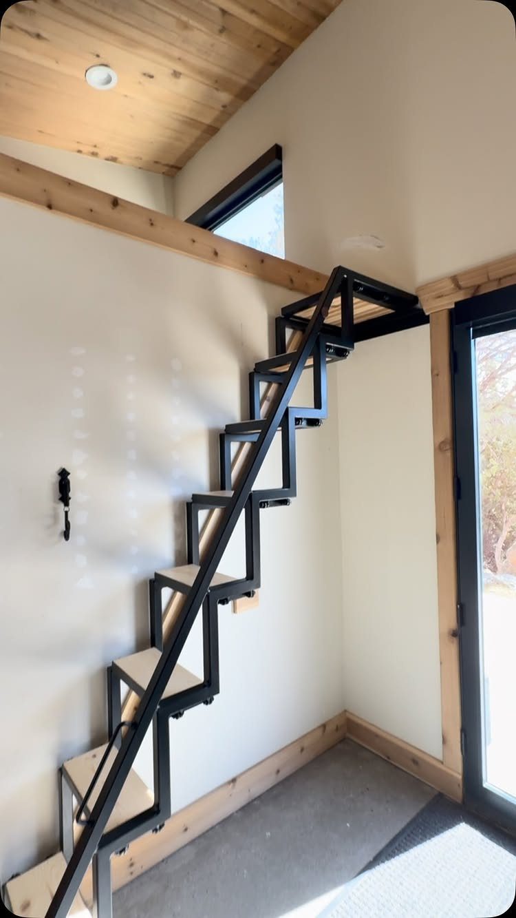 Black metal geometric stairs with light wood treads installed against a white wall.