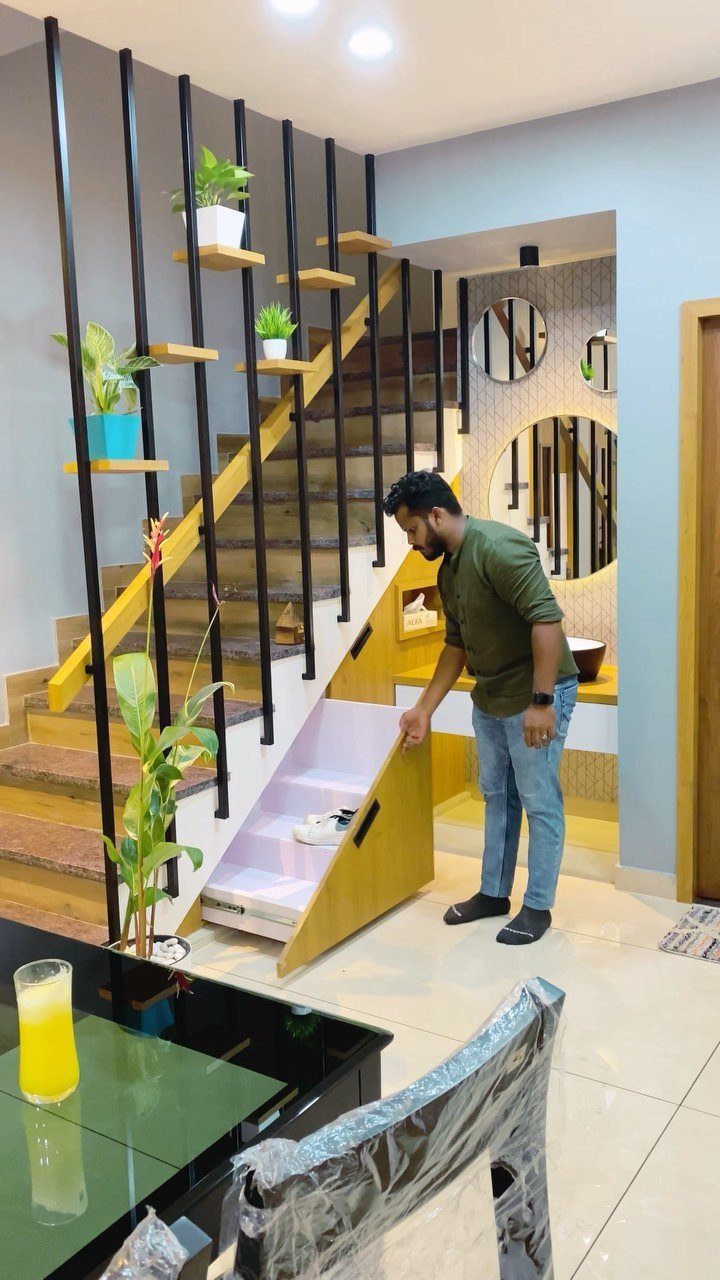 A man standing next to a wooden staircase with integrated storage drawers and black metal railings.