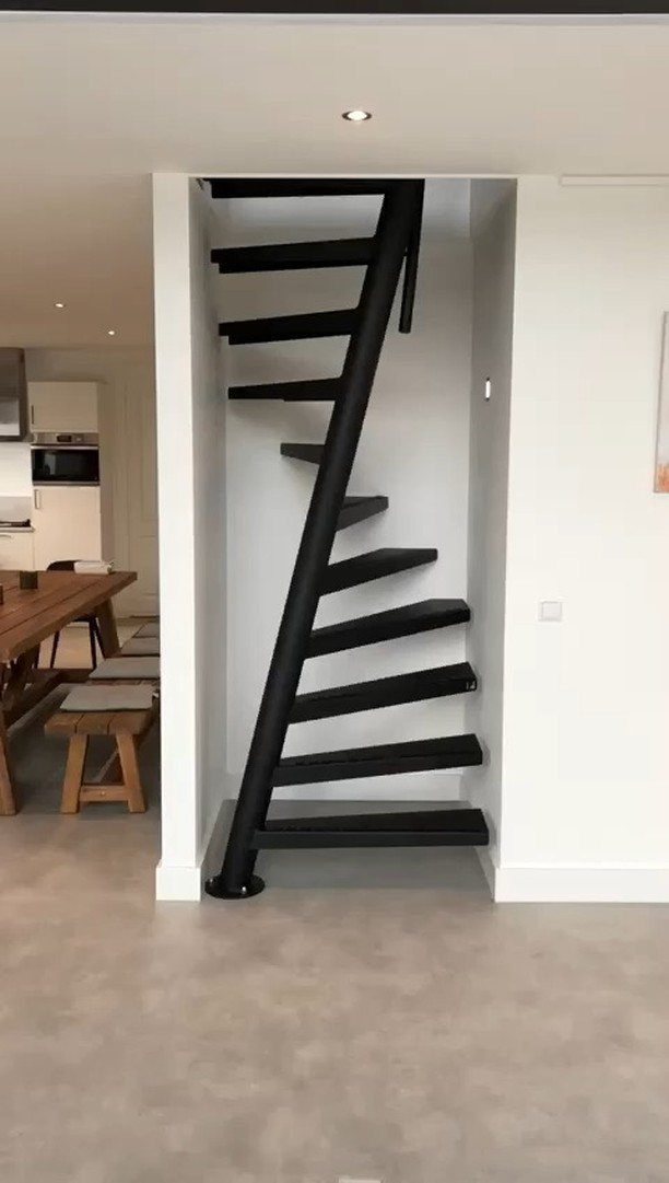Black metal spiral staircase installed in a narrow white alcove within a modern home.