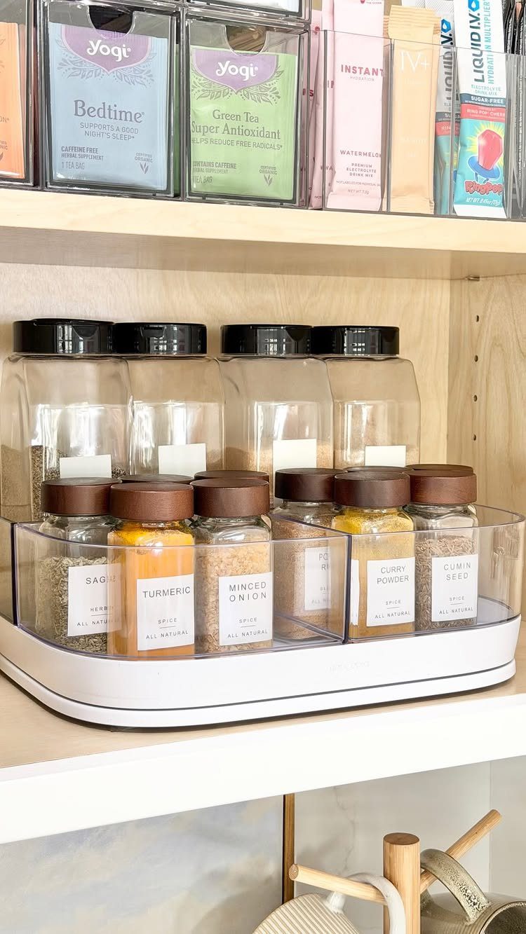 Clear spice jars with brown lids arranged in a white rotating tray on a wooden shelf.